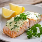 Close-up of baked salmon fillet topped with melted creamy Boursin cheese spread, garnished with chopped fresh parsley and a lemon wedge on a white plate, showcasing tender flaky pink-orange fish under a smooth white cheese topping.