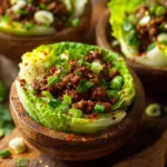 Close-up of rustic beef cabbage bowls with sautéed ground beef, green cabbage leaves, chopped green onions, sesame seeds, and red pepper flakes on a wooden surface.