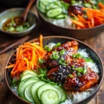 Close-up of a vibrant sweet and spicy gochujang chicken bowl with glossy pan-seared chicken thighs on white rice, fresh julienned carrots, sliced cucumber, chopped scallions, toasted sesame seeds, and cilantro leaves on a rustic wooden surface