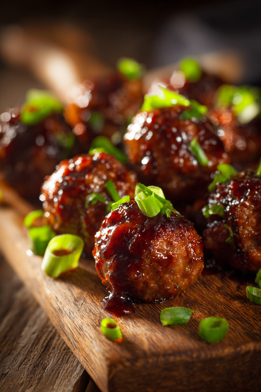 Close-up of glossy Mongolian beef meatballs on a rustic wooden board with green onions, warm natural lighting