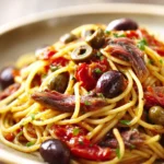 Close-up of Pasta Puttanesca with creamy sauce and herbs on a clean background.